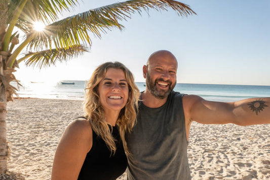 alt="Smiling couple taking a photo on the beach to capture vacation moments — a beautiful way to cherish travel memories with custom gifts